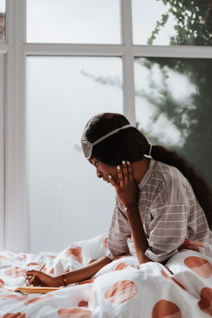 Woman in her 40s journaling in bed with a sleep mask, struggling with menopause insomnia and night sweats 